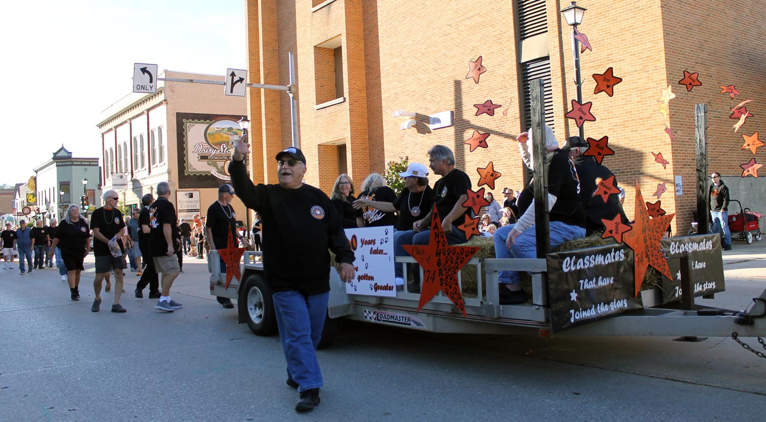 alumni riding and walking next to trailer