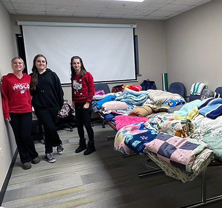 3 students with blankets piled on table