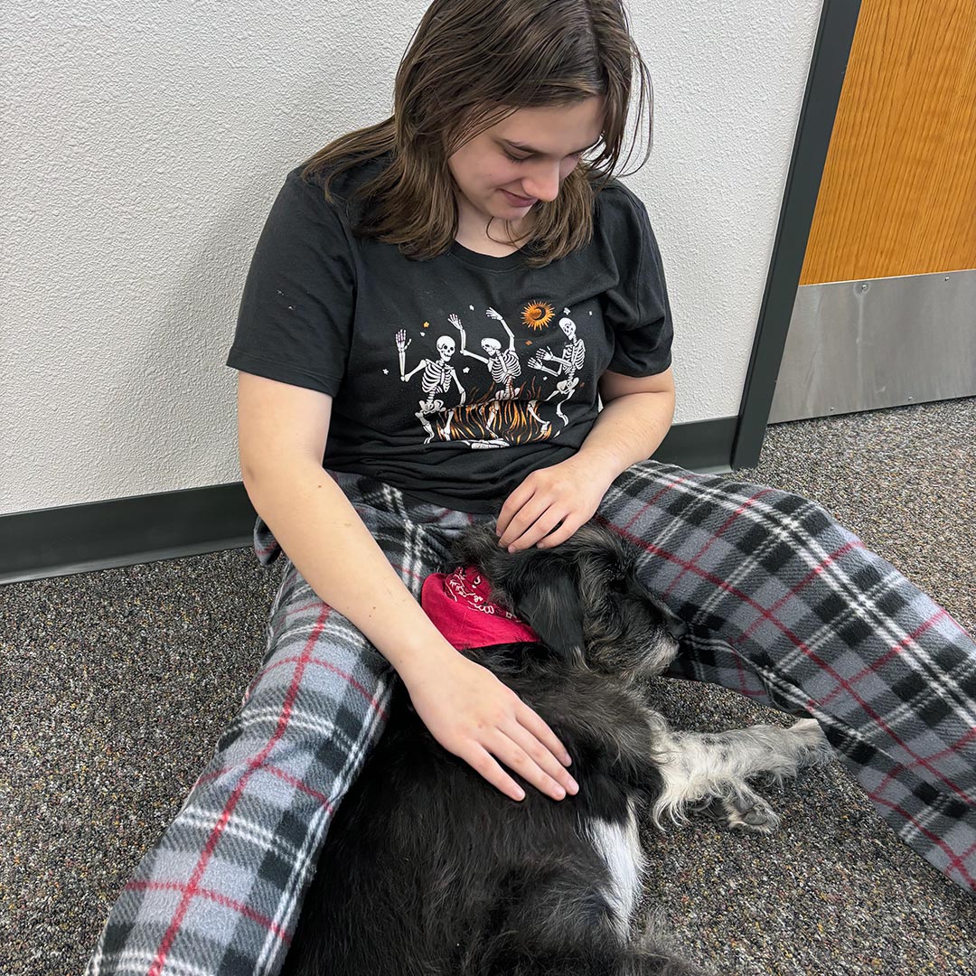 student sitting and petting dog lying on floor