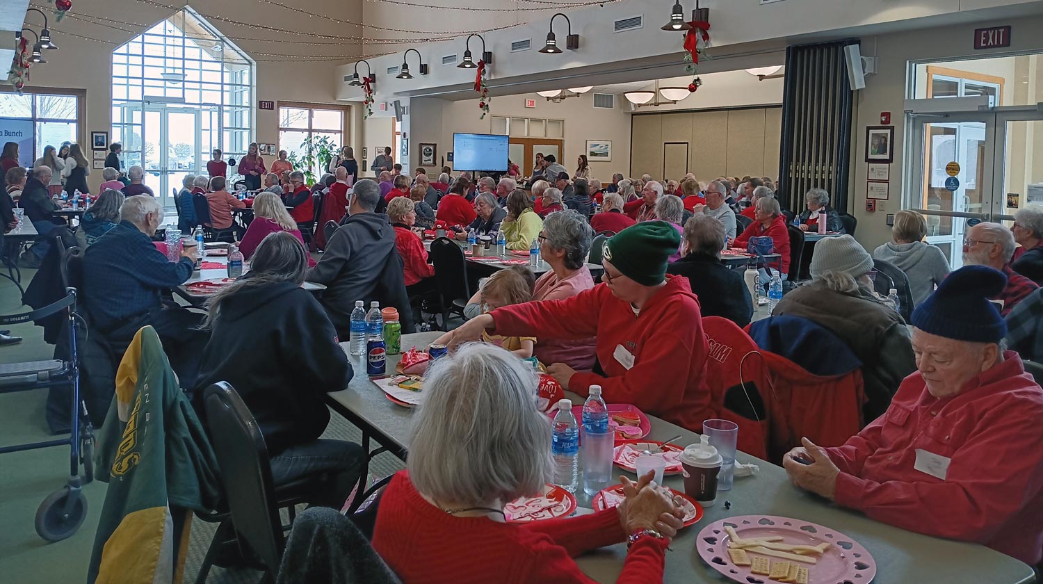 A large group of people seated at tables in a decorated room, wearing predominantly red clothing.