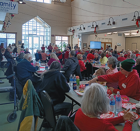 A large group of people seated at tables in a decorated room, wearing predominantly red clothing