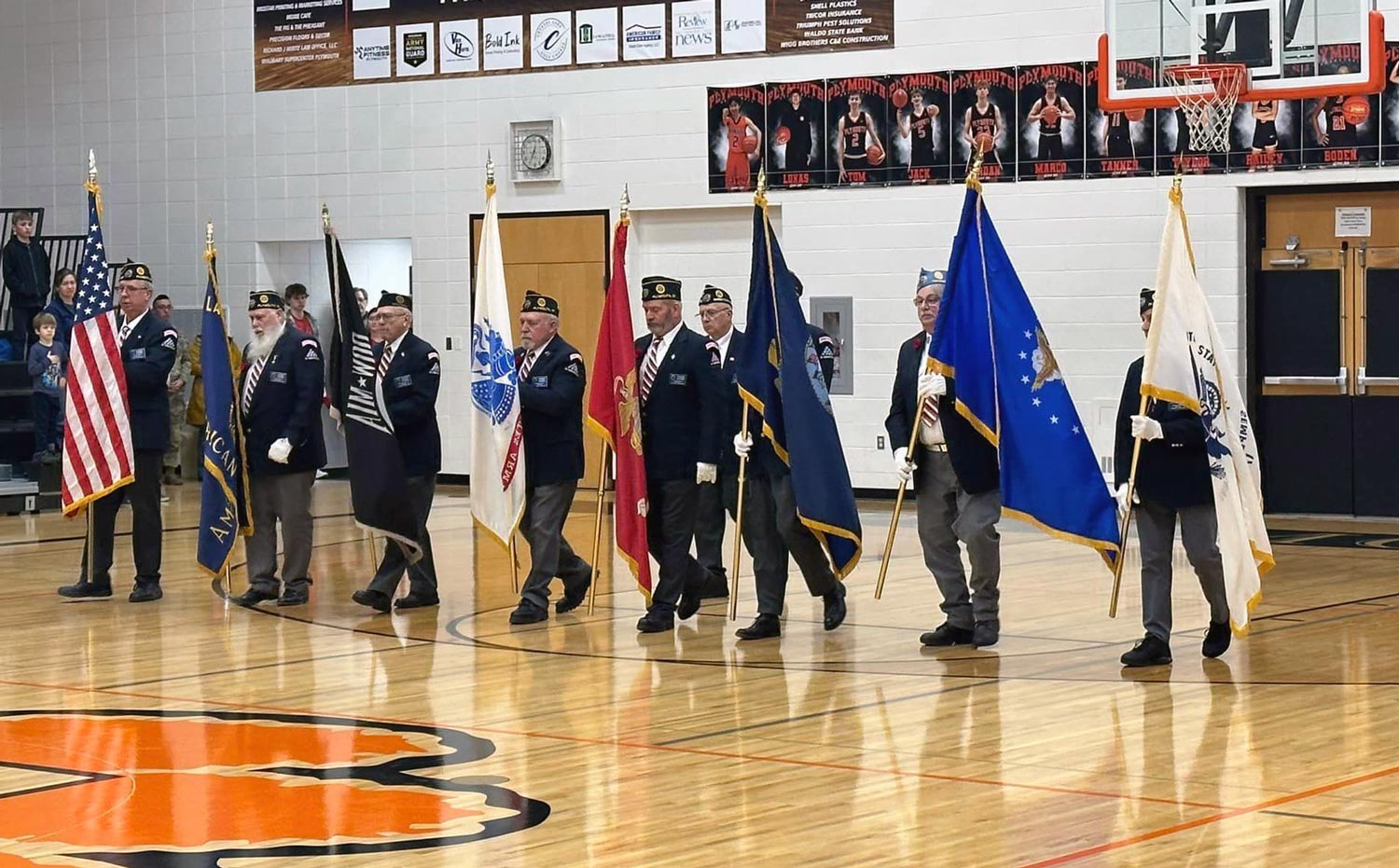 Veterans in uniform carry flags in the PHS gym.