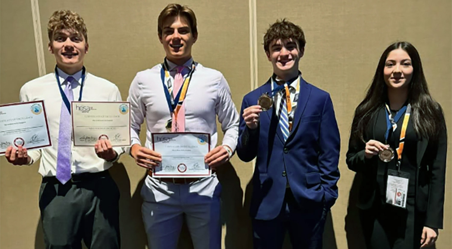 four students wearing medals, two of whom are also holding certificates 