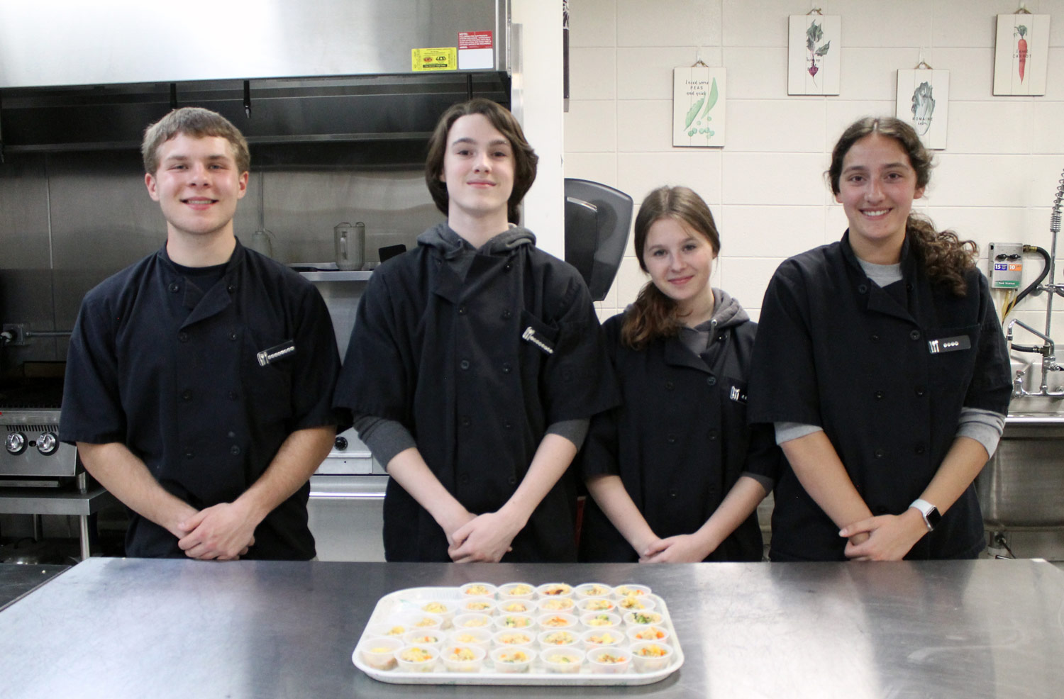 4 students in chef uniforms standing behind samples of their dish