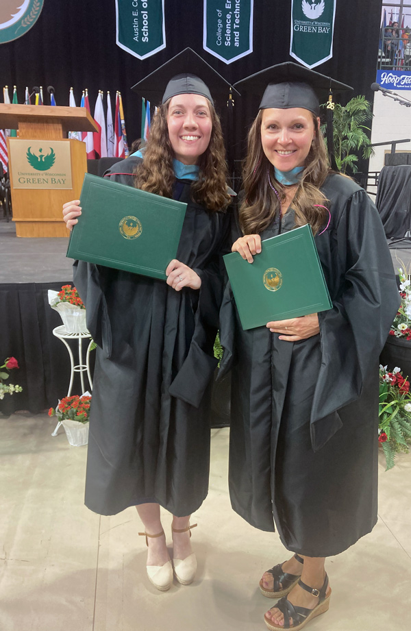 2 teachers in caps and gowns holding diplomas