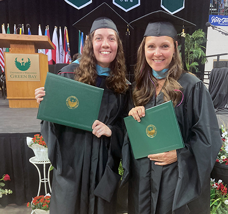 2 teachers in cap and gown holding diplomas