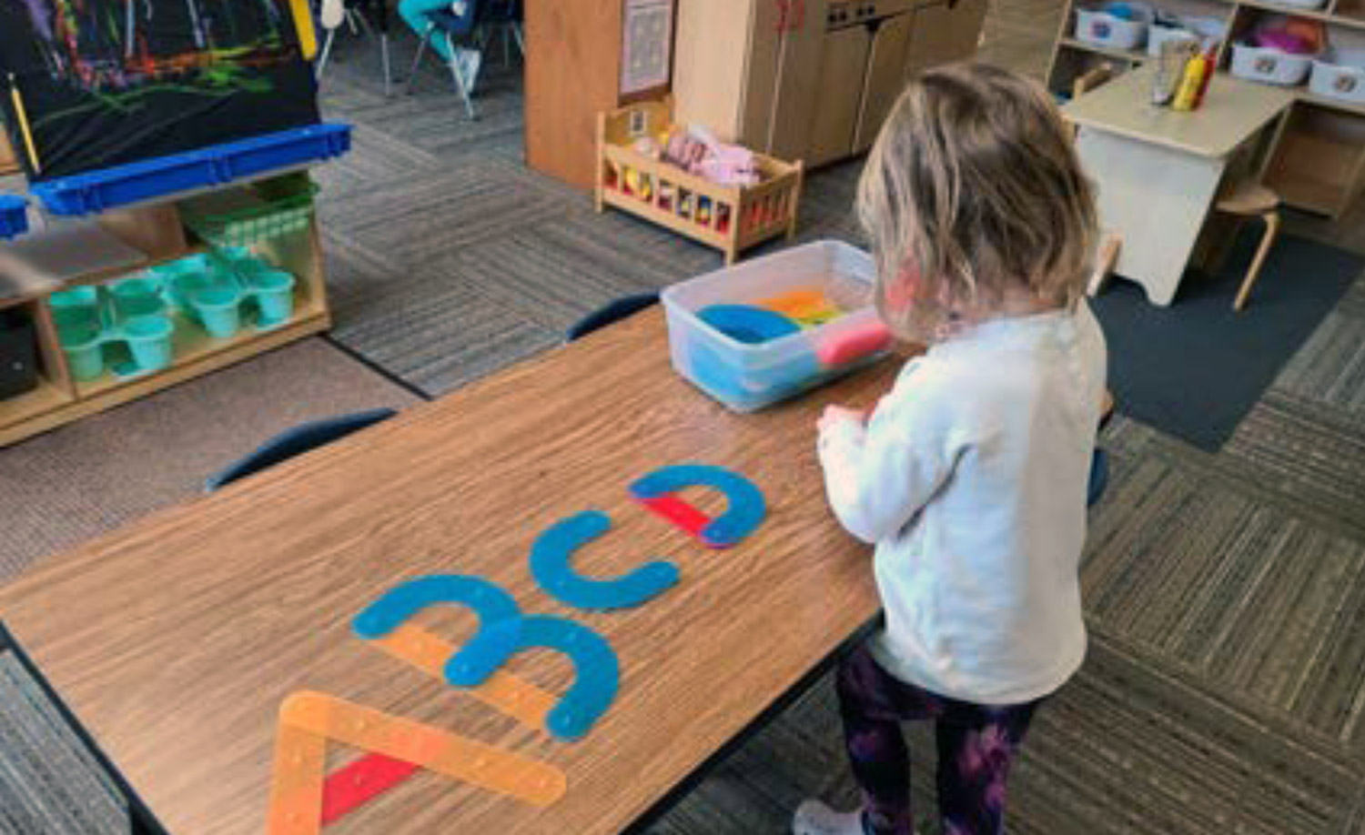 A student forms letter shapes on a classroom table
